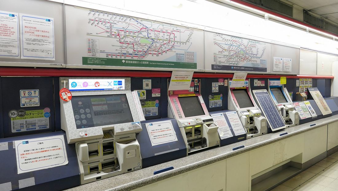A row of ticket machines along a subway station wall, with the fare map mounted above them.