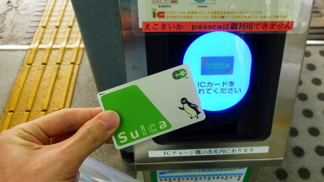 A hand holding an IC card flat against the glowing reader panel of a ticket gate.